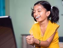 Young girl wearing a bright yellow shirt and smiling at a computer screen