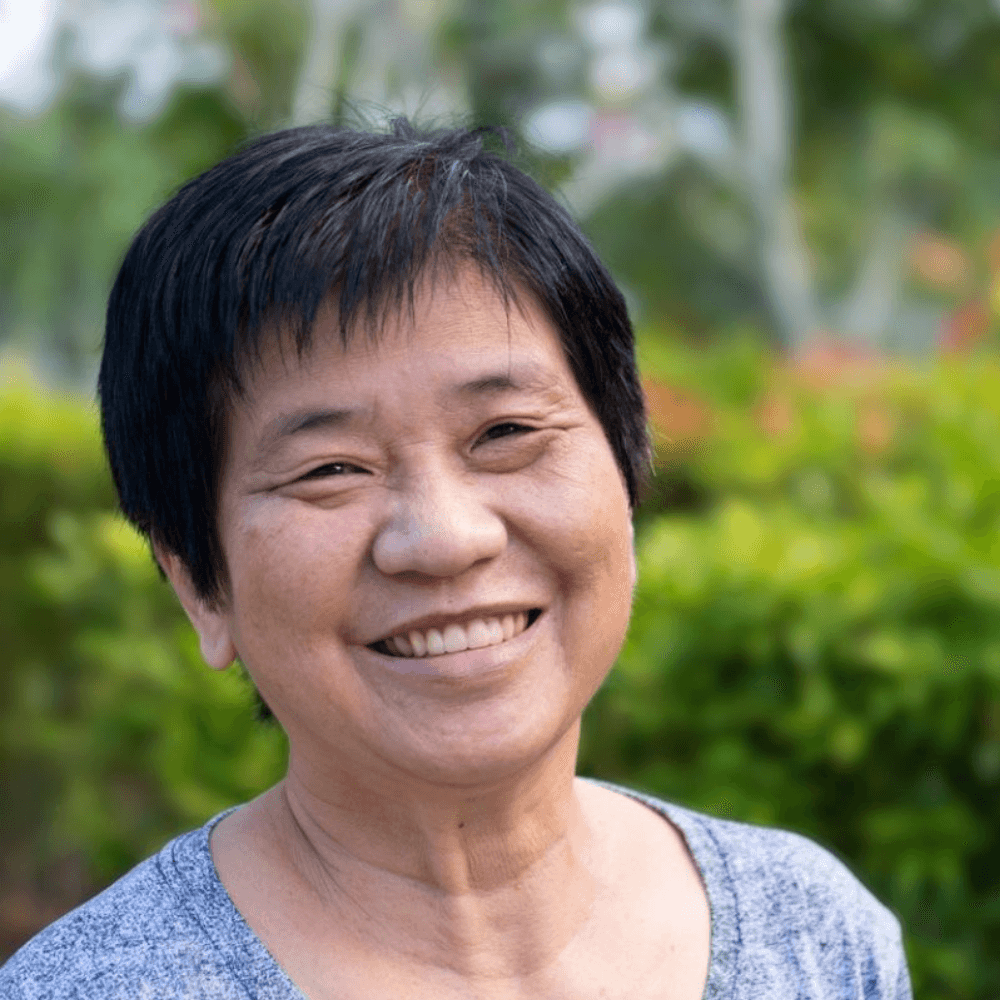 Older lady with an Asian ethnicity smiling in a green outdoor setting